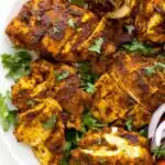 Sliced chicken shawarma on a white plate drizzled with creamy garlic sauce and topped with fresh parsley