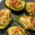Golden chicken-stuffed baked avocados with melted Parmesan on a white ceramic plate