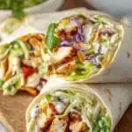 Chipotle Chicken Wraps 6 Chipotle chicken wraps sliced in half on a wooden board with chipotle lime yogurt sauce drizzled over the top