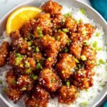 Copycat Panda Express Orange Chicken recipe served over white rice with sesame seeds and green onions in a bowl