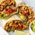 Easy Chicken Burrito 6 Easy chicken burrito recipe cut in half showing shredded chicken, black beans, and guacamole filling on a wooden board