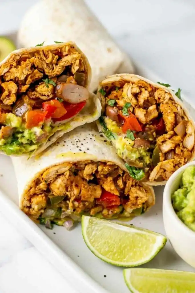 Easy Chicken Burrito 5 Easy chicken burrito recipe cut in half showing shredded chicken, black beans, and guacamole filling on a wooden board