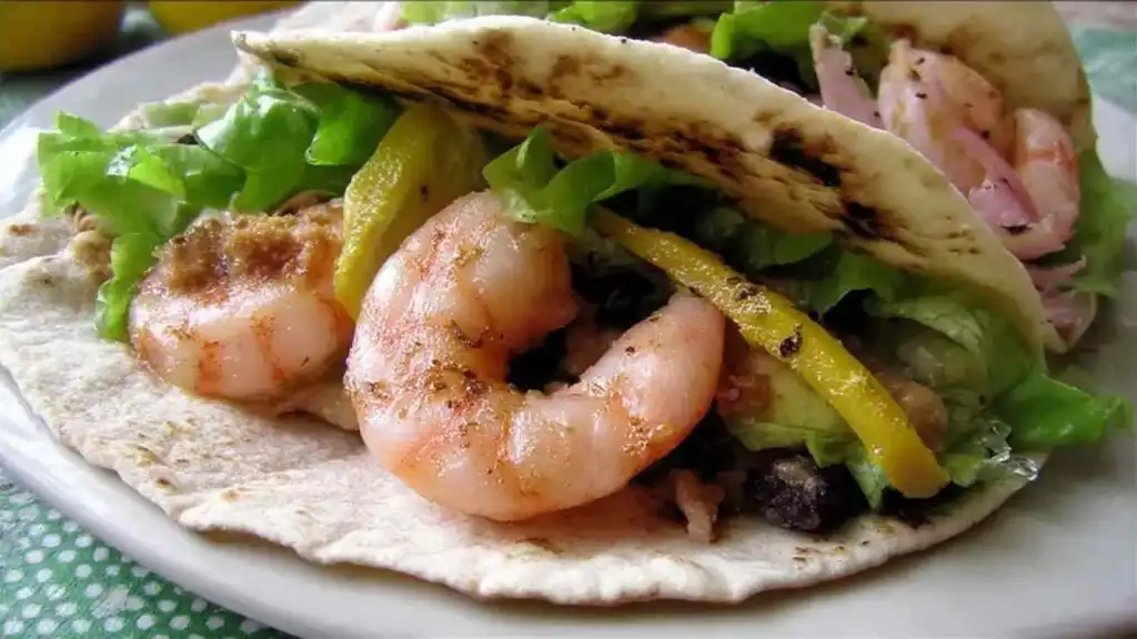 Grilled Shrimp Tacos 1 Three grilled shrimp tacos on a white plate topped with creamy taco ranch sauce, fresh salad greens, and crunchy chips