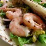 Grilled Shrimp Tacos 3 Three grilled shrimp tacos on a white plate topped with creamy taco ranch sauce, fresh salad greens, and crunchy chips