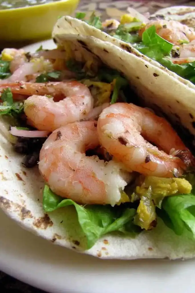 Grilled Shrimp Tacos 2 Three grilled shrimp tacos on a white plate topped with creamy taco ranch sauce, fresh salad greens, and crunchy chips