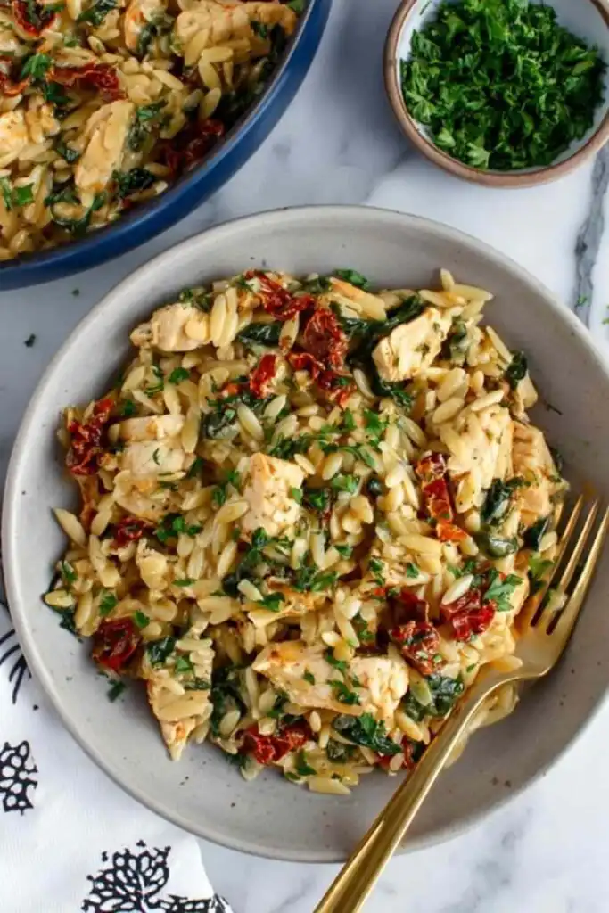 Mediterranean Chicken and Orzo 29 Mediterranean chicken and orzo with spinach and sundried tomatoes in a large skillet garnished with fresh parsley