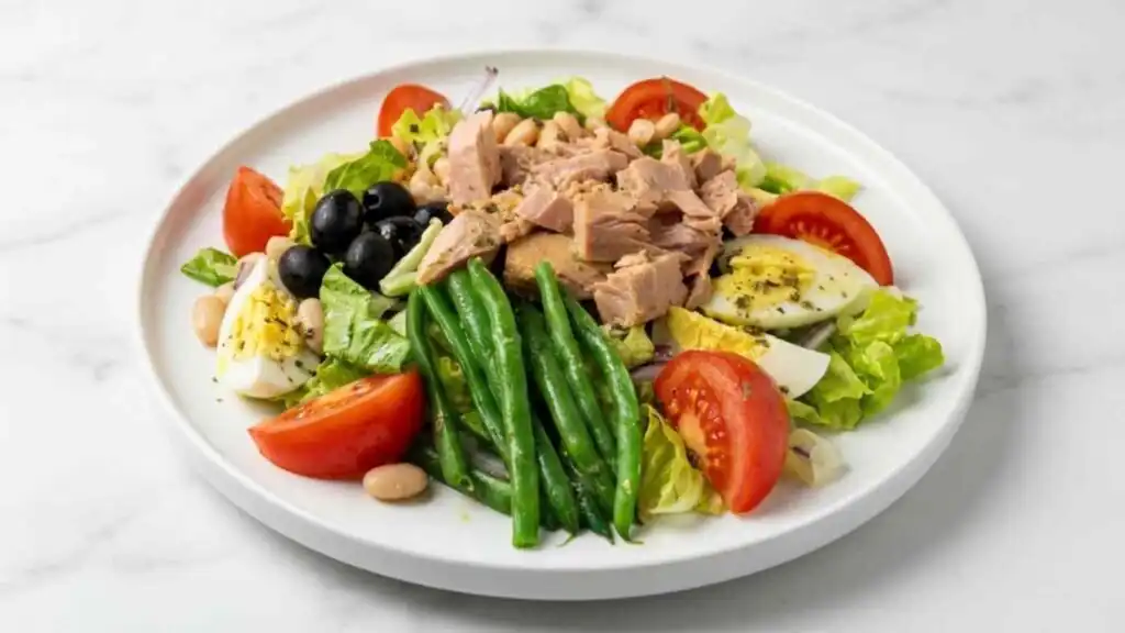Nicoise-Style Tuna Salad With White Beans and Olives 16 Overhead view of nicoise-style tuna salad with white beans and olives served on a white plate with steamed green beans and quartered hard-boiled eggs