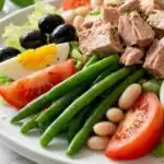 Nicoise-Style Tuna Salad With White Beans and Olives 18 Overhead view of nicoise-style tuna salad with white beans and olives served on a white plate with steamed green beans and quartered hard-boiled eggs