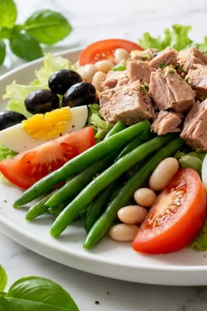 Nicoise-Style Tuna Salad With White Beans and Olives 17 Overhead view of nicoise-style tuna salad with white beans and olives served on a white plate with steamed green beans and quartered hard-boiled eggs