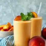 High Protein Peach Smoothie 21 Creamy high protein peach smoothie in a tall glass topped with fresh peach slices on a light wooden surface