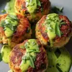 Golden baked salmon balls with creamy avocado sauce on a white serving plate garnished with fresh dill