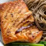 Salmon Soba Noodle Salad 24 Salmon soba noodle salad with crispy skin salmon, buckwheat soba noodles, blanched spinach, and ginger dressing in a white bowl