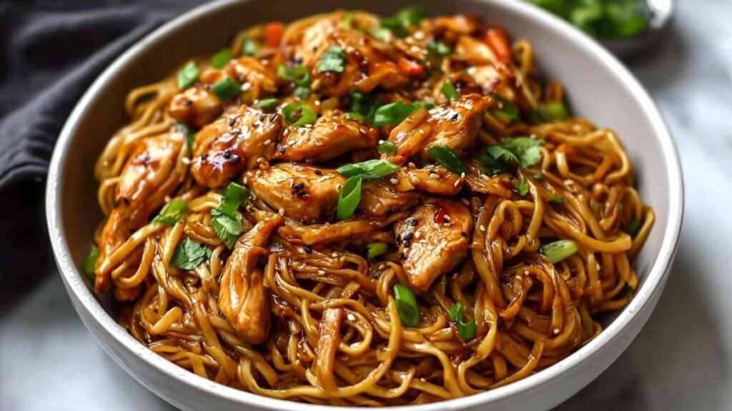 High Protein Sticky Garlic Chicken Noodles in a skillet topped with sesame seeds and green onions
