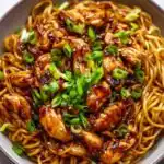High Protein Sticky Garlic Chicken Noodles in a skillet topped with sesame seeds and green onions