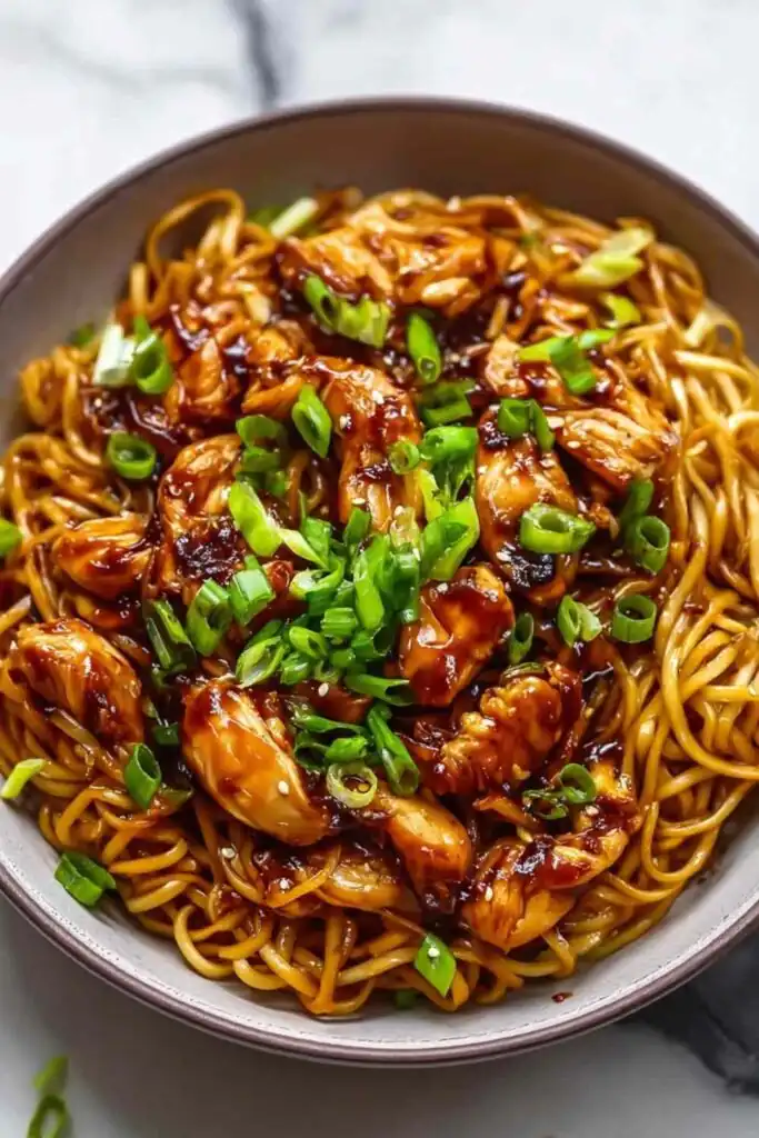 High Protein Sticky Garlic Chicken Noodles in a skillet topped with sesame seeds and green onions