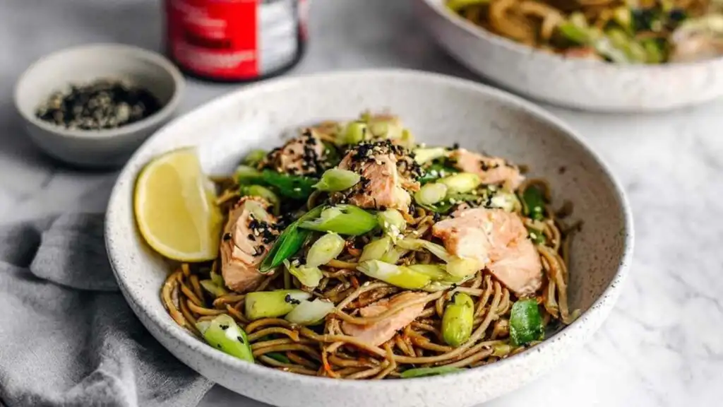 Sesame ginger soba noodle bowl with salmon topped with sesame seeds and scallions served in a white bowl