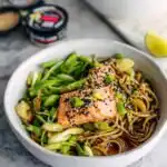 Sesame ginger soba noodle bowl with salmon topped with sesame seeds and scallions served in a white bowl