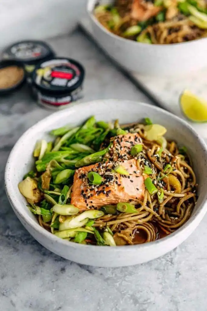 Sesame ginger soba noodle bowl with salmon topped with sesame seeds and scallions served in a white bowl