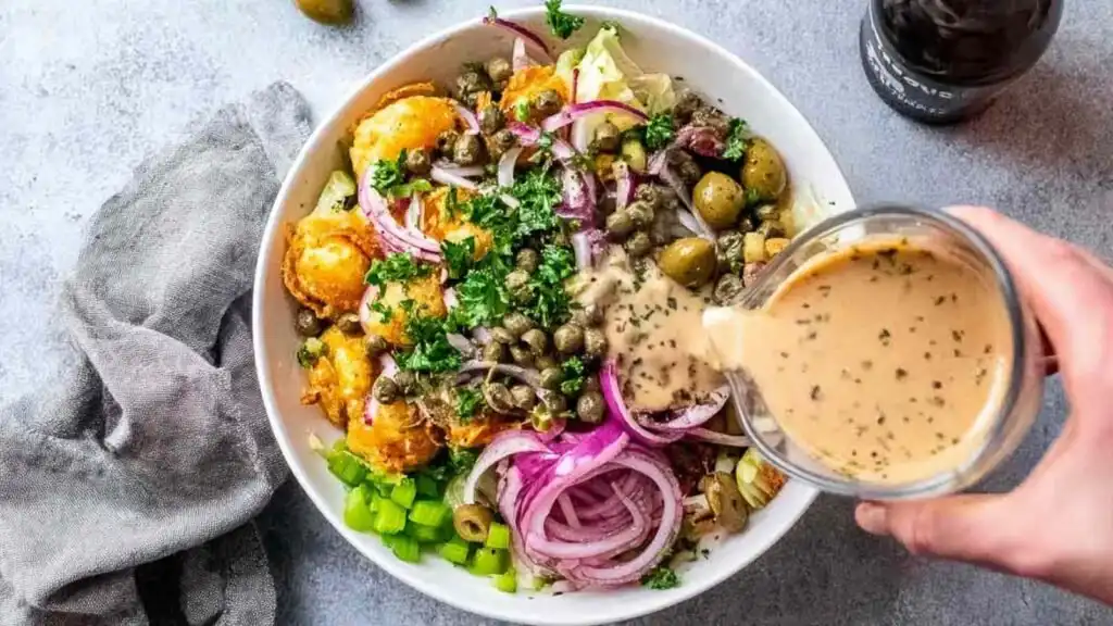 High protein smashed potato salad with grilled lemon garlic chicken, olives, capers, and tahini dressing served in a large bowl