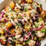 High protein smashed potato salad with grilled lemon garlic chicken, olives, capers, and tahini dressing served in a large bowl