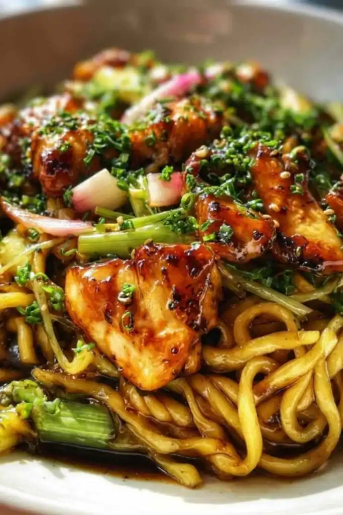 Sticky garlic chicken noodles in a cast iron skillet with bright green broccolini and toasted sesame seeds