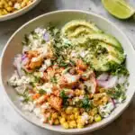 Street Corn Chicken Bowls 15 Overhead view of a Street Corn Chicken Bowl with charred corn, sliced chicken, avocado, crumbled cotija, and cilantro over white rice with tajin-lime sauce