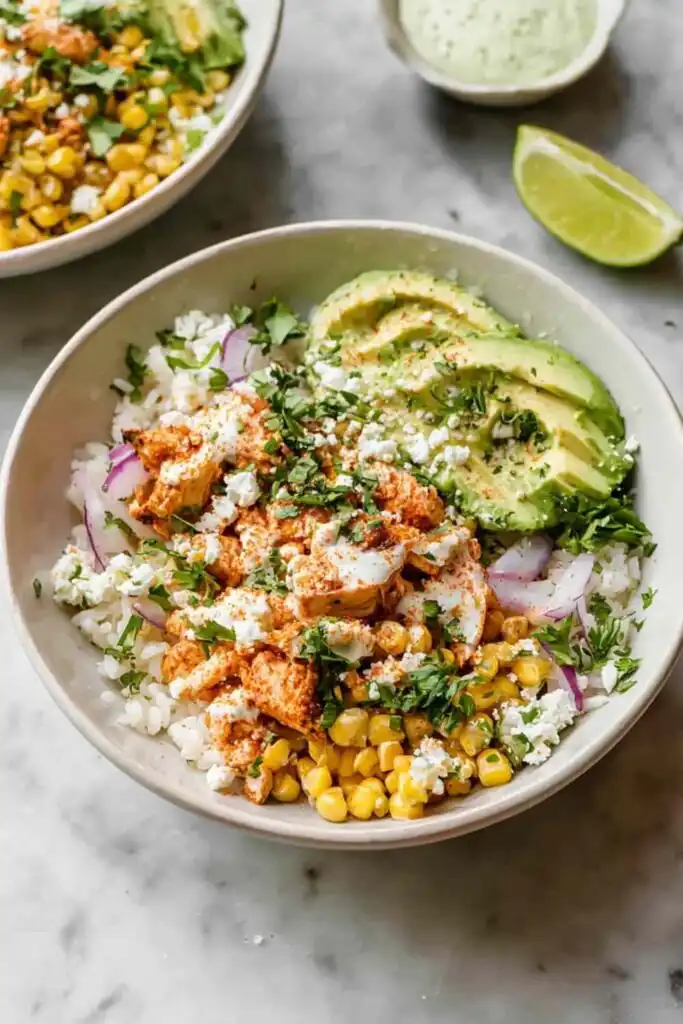 Street Corn Chicken Bowls 14 Overhead view of a Street Corn Chicken Bowl with charred corn, sliced chicken, avocado, crumbled cotija, and cilantro over white rice with tajin-lime sauce