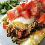 Four taco-stuffed zucchini boats in a baking dish topped with melted cheddar and Muenster cheese and dollops of seasoned sour cream