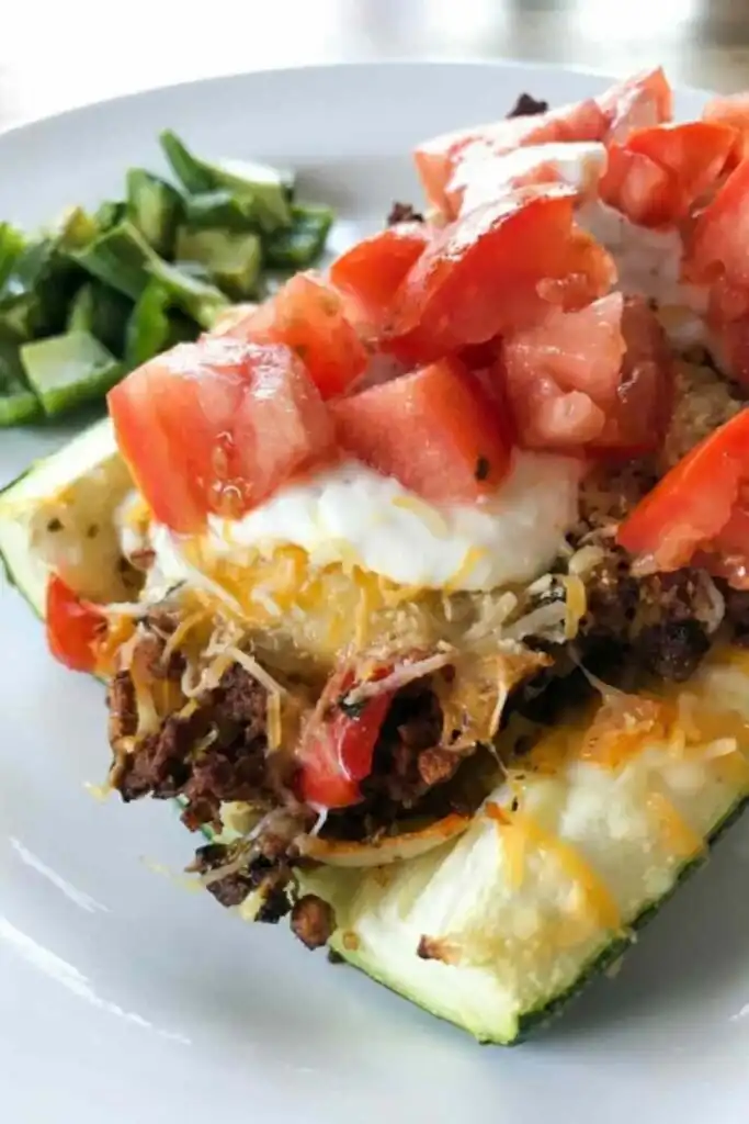 Four taco-stuffed zucchini boats in a baking dish topped with melted cheddar and Muenster cheese and dollops of seasoned sour cream