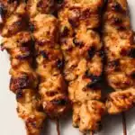 Tahini chicken skewers served on a white platter garnished with toasted sesame seeds and sliced green onions